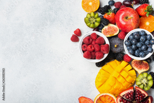 Healthy raw rainbow fruits, mango papaya strawberries oranges passion fruits berries on oval serving plate on light kitchen top, top view, copy space, selective focus