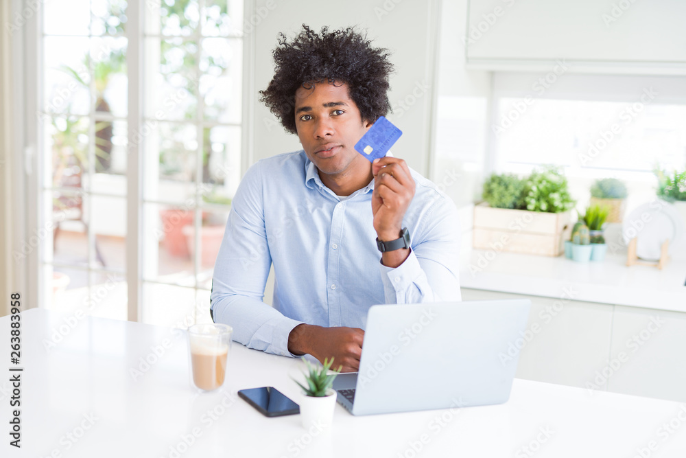 African American man using laptop and shopping online with credit card with a confident expression on smart face thinking serious African American man using laptop and shopping online with credit card with a confident expression on smart face thinking serious