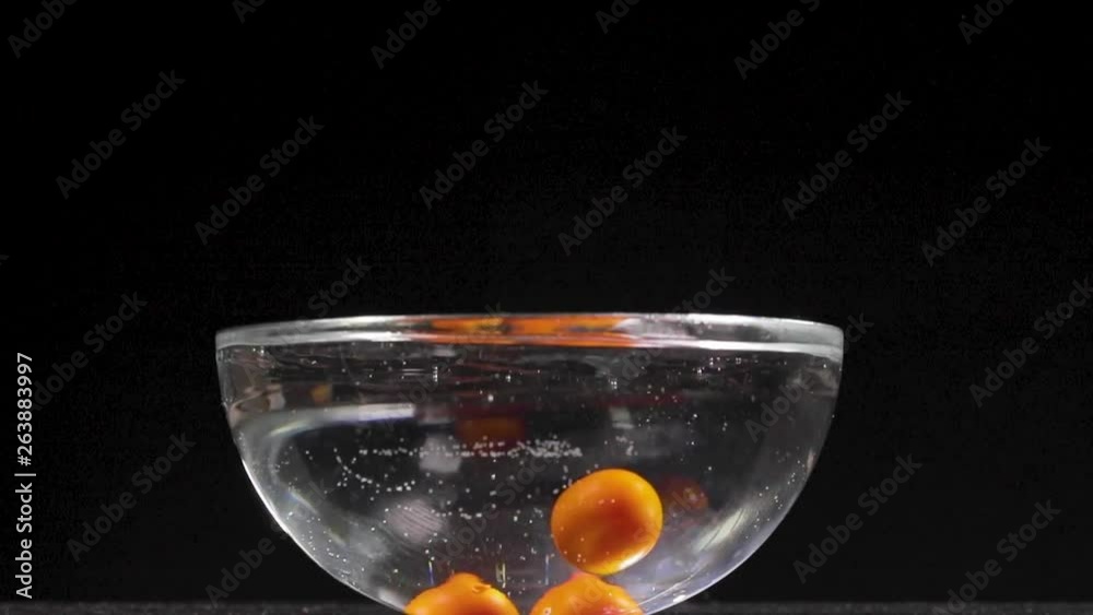 Pomodorini per sugo rosso cadono in una bacinella piena d'acqua facendo schizzi. Sfondo nero, video al rallentatore.