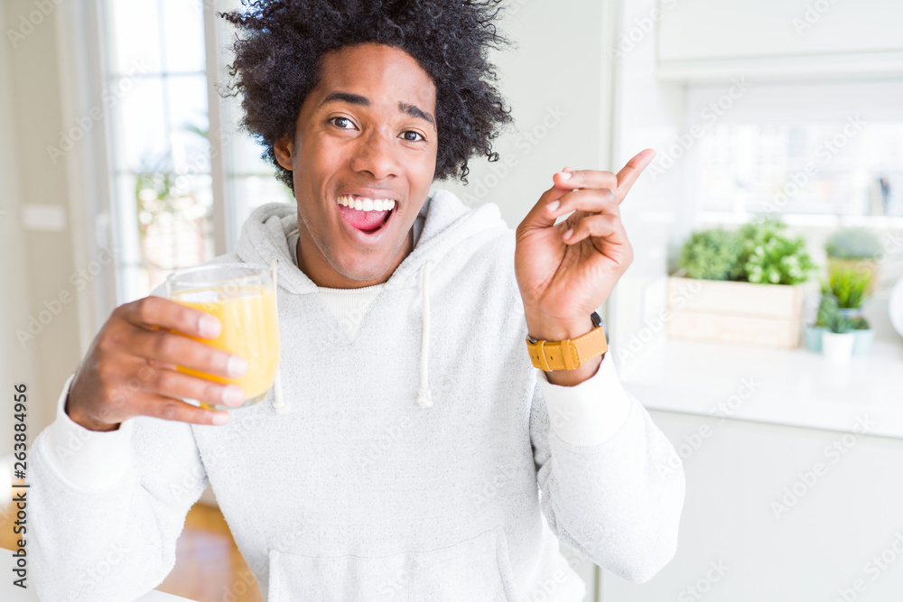 African American man holding and drinking glass of orange juice very happy pointing with hand and finger to the side