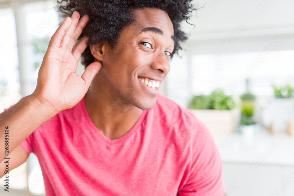 African American business man wearing pink casual t-shirt smiling with hand over ear listening an hearing to rumor or gossip. Deafness concept. African American business man wearing pink casual t-shirt smiling with hand over ear listening an hearing to rumor or gossip. Deafness concept.
