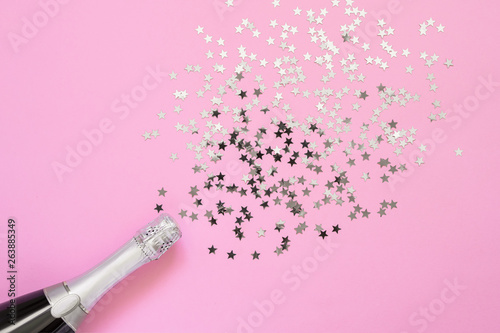 Champagne bottle with confetti stars on bright pink background. Copy space, top view