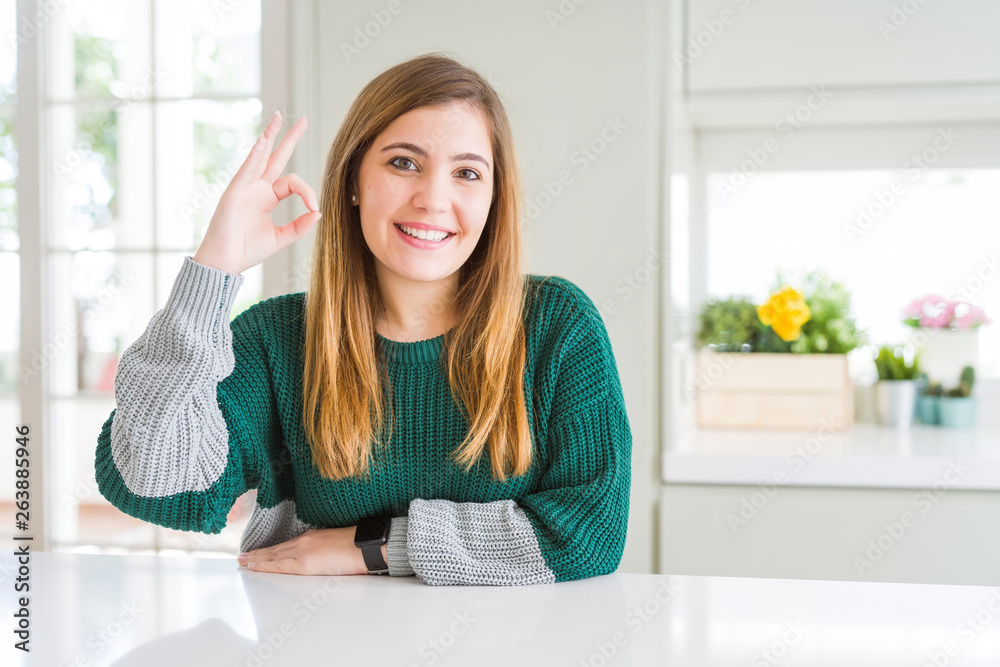 Young beautiful plus size woman wearing casual striped sweater smiling positive doing ok sign with hand and fingers. Successful expression.