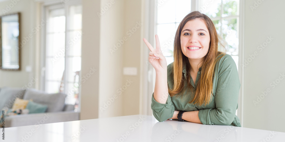 Beautiful young woman at home smiling with happy face winking at the camera doing victory sign. Number two.