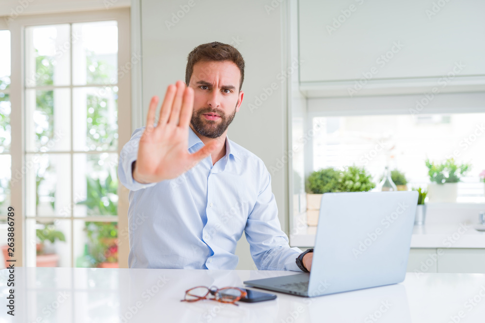 Handsome business man working using computer laptop with open hand doing stop sign with serious and confident expression, defense gesture
