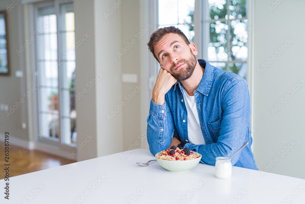 Handsome man eating cereals for breakfast at home with hand on chin thinking about question, pensive expression. Smiling with thoughtful face. Doubt concept. Handsome man eating cereals for breakfast at home with hand on chin thinking about question, pensive expression. Smiling with thoughtful face. Doubt concept.