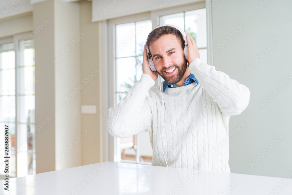 Handsome man wearing headphones and listening to music with a happy face standing and smiling with a confident smile showing teeth