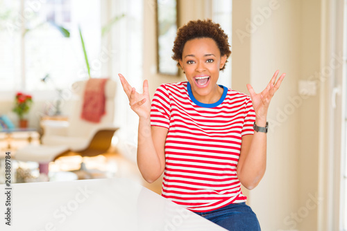 Young beautiful african american woman at home celebrating crazy and amazed for success with arms raised and open eyes screaming excited. Winner concept