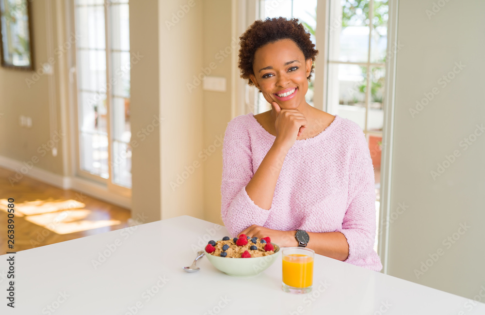 Young african american woman having healthy breakfast in the morning at home looking confident at the camera with smile with crossed arms and hand raised on chin. Thinking positive. Young african american woman having healthy breakfast in the morning at home looking confident at the camera with smile with crossed arms and hand raised on chin. Thinking positive.