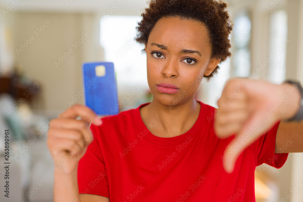 Young african american woman holding credit card with angry face, negative sign showing dislike with thumbs down, rejection concept Young african american woman holding credit card with angry face, negative sign showing dislike with thumbs down, rejection concept