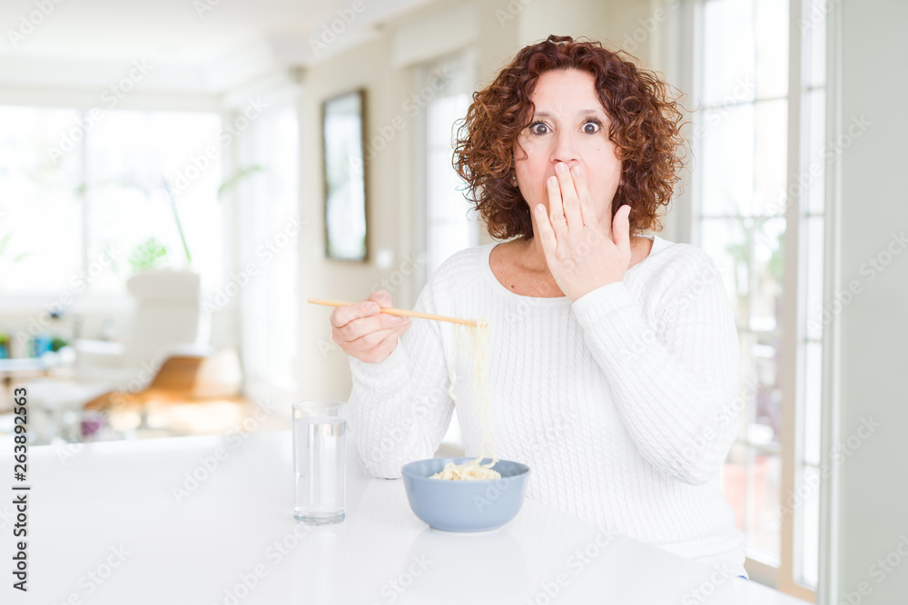 Senior woman eating asian noodles using chopsticks cover mouth with hand shocked with shame for mistake, expression of fear, scared in silence, secret concept Senior woman eating asian noodles using chopsticks cover mouth with hand shocked with shame for mistake, expression of fear, scared in silence, secret concept