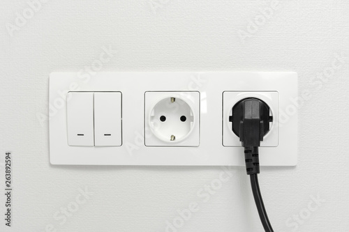 Electrical sockets on the wall with black connection plug and white switch.