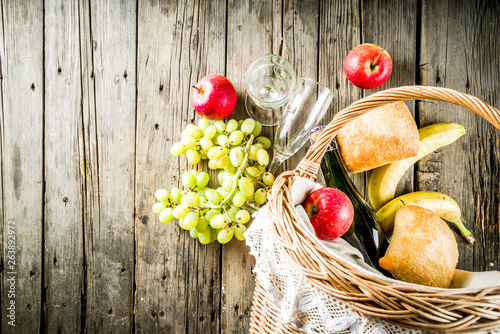 Picnic basket with food and drinks (fresh fruits, bread and wine bottle, glasses), copy space photo