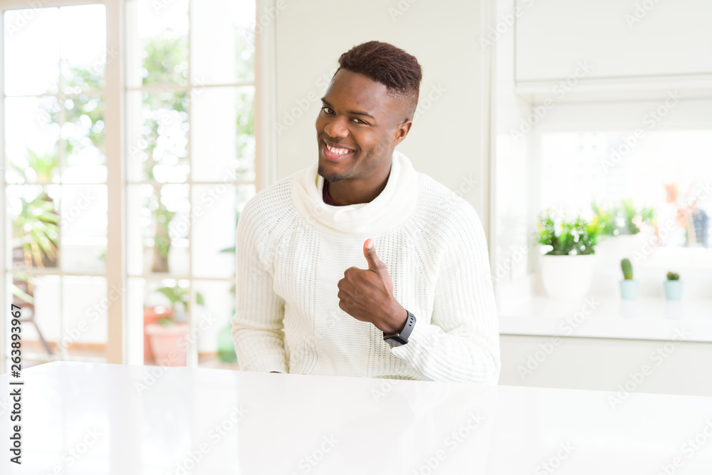 Handsome african american man on white table doing happy thumbs up gesture with hand. Approving expression looking at the camera showing success.