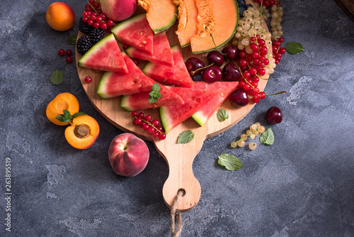 Bild auf Leinwand Fresh summer fruits and berries on a round cutting board, watermelon, cantaloupe