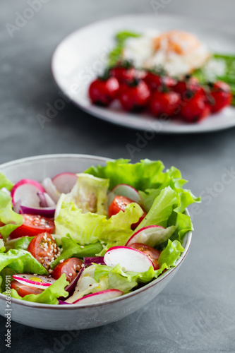 Healthy classical vegetable fresh salad of lettuce, tomato, cucumber, onion and sesame with olive oil dressing on white plate and white background. Diet menu.