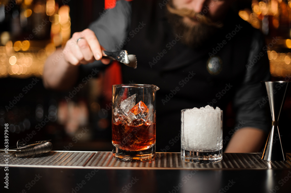 Bartender adds ice in glass with ice tongs