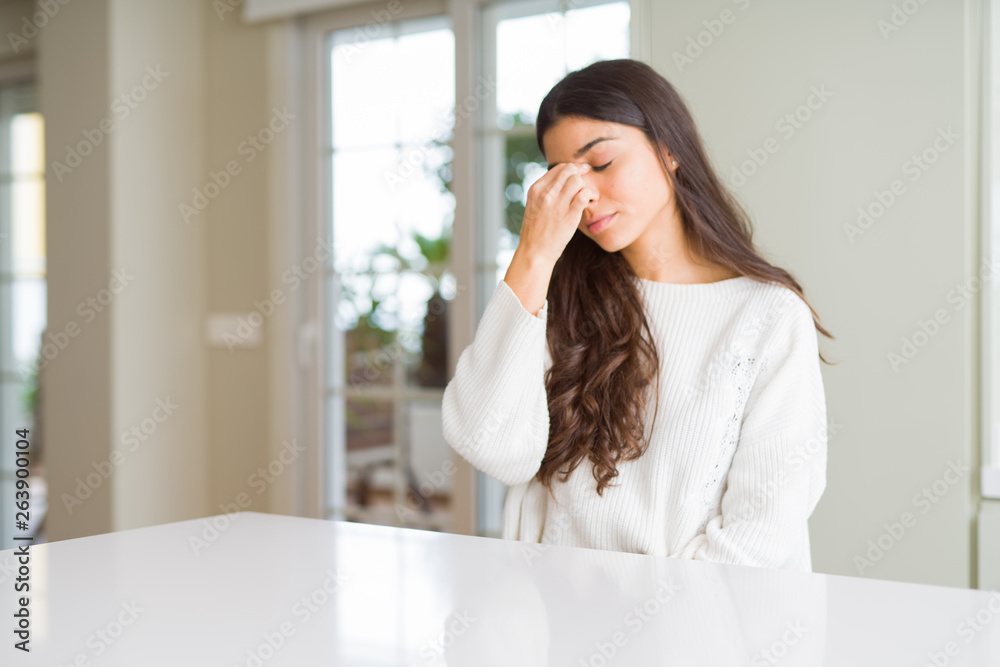 Young beautiful woman at home on white table tired rubbing nose and eyes feeling fatigue and headache. Stress and frustration concept. Young beautiful woman at home on white table tired rubbing nose and eyes feeling fatigue and headache. Stress and frustration concept.