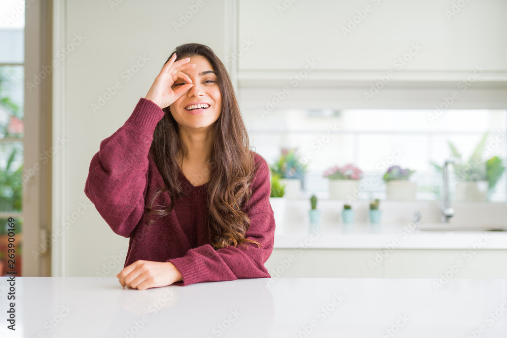 Young beautiful woman at home doing ok gesture with hand smiling, eye looking through fingers with happy face. Young beautiful woman at home doing ok gesture with hand smiling, eye looking through fingers with happy face.