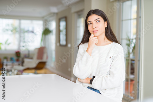 Young beautiful woman at home on white table with hand on chin thinking about question, pensive expression. Smiling with thoughtful face. Doubt concept. Free Download Young beautiful woman at home on white table with hand on chin thinking about question, pensive expression. Smiling with thoughtful face. Doubt concept. - GFXLoad