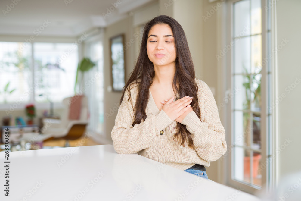 Young beautiful woman at home smiling with hands on chest with closed eyes and grateful gesture on face. Health concept. Young beautiful woman at home smiling with hands on chest with closed eyes and grateful gesture on face. Health concept.