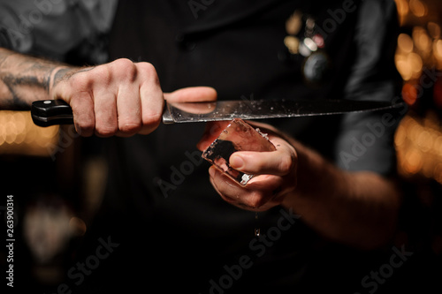 Close shot of bartender cutting ice with a knife