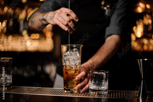 Male bartender stirring alcohol cocktail with bar spoon