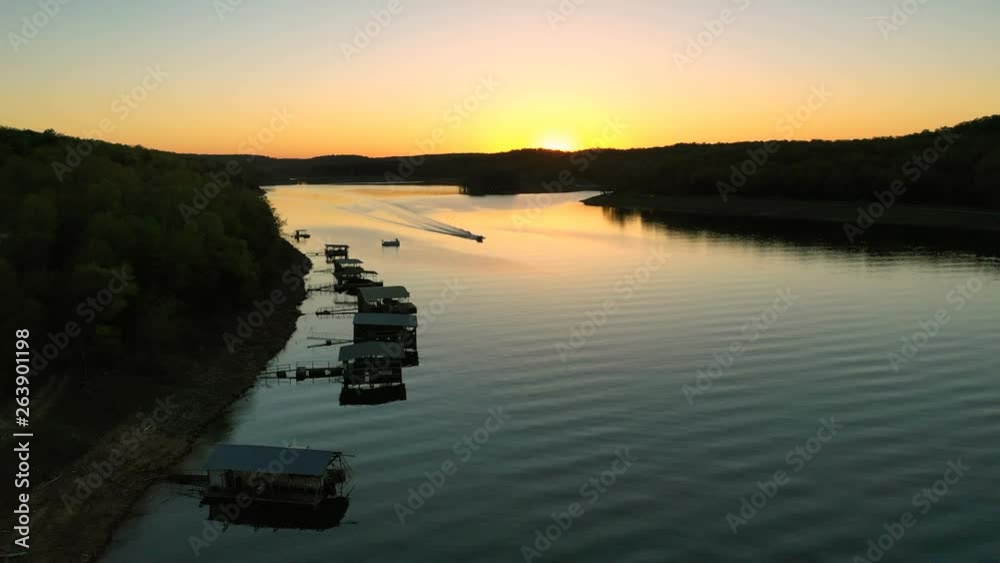 A drone pass into the sunset over some boat docks as a pleasure boat passes underneath. Video was taken on Lake Norfork near Mountain Home Arkansas. A drone pass into the sunset over some boat docks as a pleasure boat passes underneath. Video was taken on Lake Norfork near Mountain Home Arkansas.