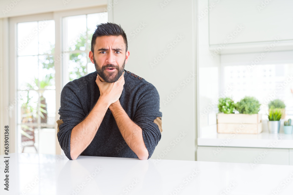 Handsome hispanic man wearing casual sweater at home shouting and suffocate because painful strangle. Health problem. Asphyxiate and suicide concept. Handsome hispanic man wearing casual sweater at home shouting and suffocate because painful strangle. Health problem. Asphyxiate and suicide concept.