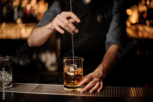 Male bartender stirs alcohol cocktail with bar spoon