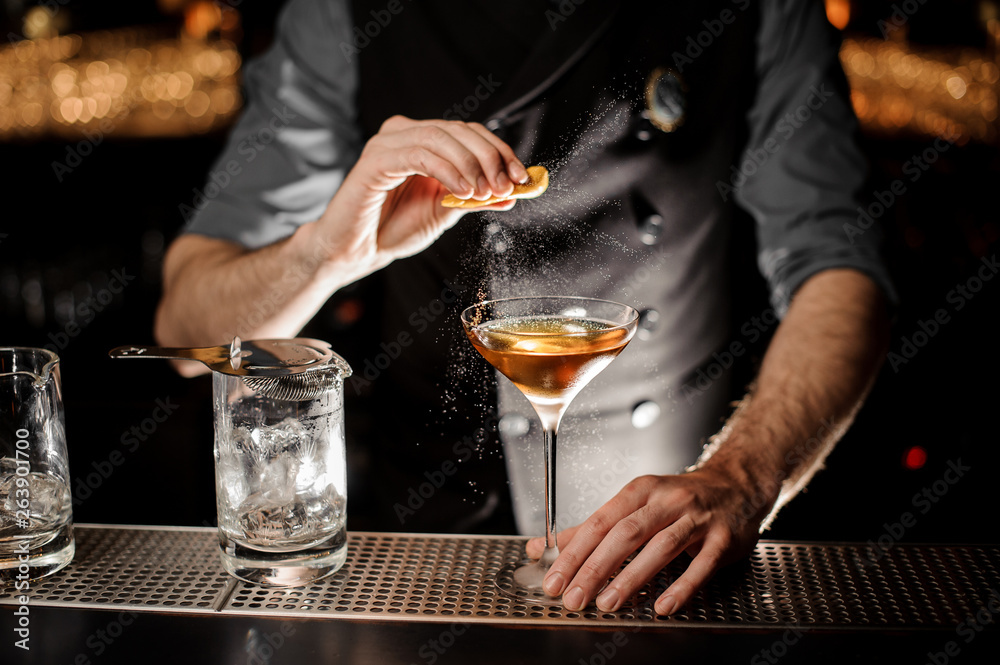 Bartender squeezing lemon rind in alcohol cocktail