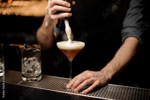 Bartender pours an alcohol cocktail adding foam