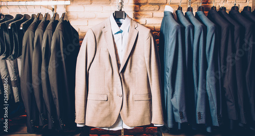 Men formal wear. Classy outfit. Modern clothing store. Business suit jackets and vests hanging, displayed over brick wall. photo