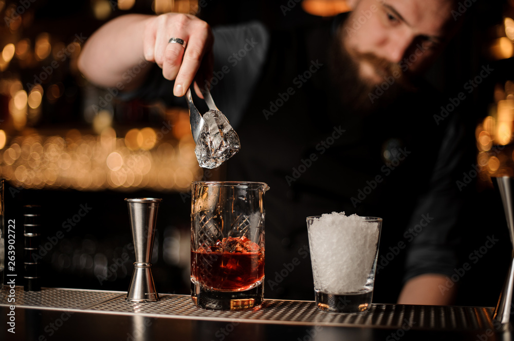 Bartender adds ice in glass with special ice tongs