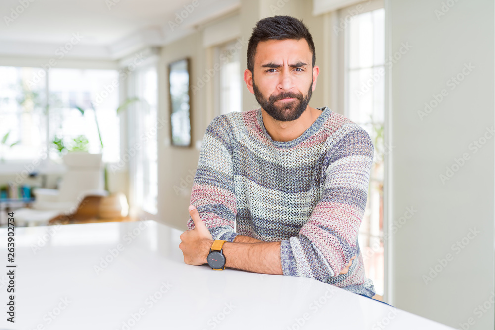 Handsome hispanic man wearing casual sweater at home skeptic and nervous, disapproving expression on face with crossed arms. Negative person.