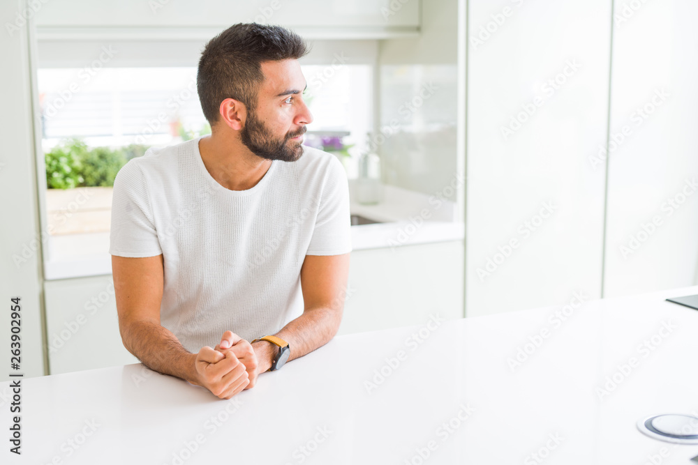Handsome hispanic man casual white t-shirt at home looking to side, relax profile pose with natural face with confident smile.