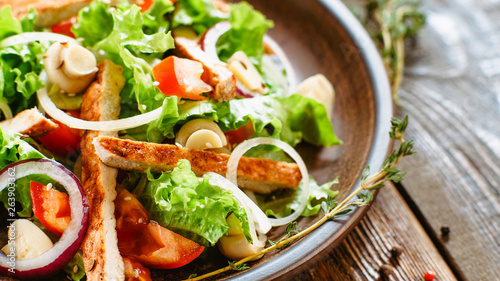 Restaurant kitchen menu. Cropped closeup of chicken salad with vegetables. Served in rustic clay plate on wooden table.