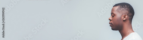 Meditation and relaxation. Side view portrait of concentrated african man with closed eyes on grey background. Empty space.
