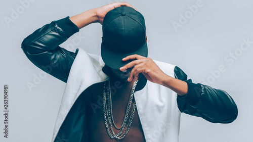 Afro american urban guy. Rapper posing in cap and leather jacket on naked torso. Head tilted down. Rap culture lifestyle. photo