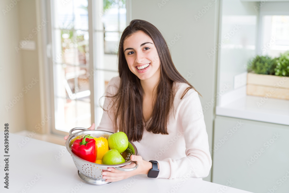 Beautiful young woman using colander to wash and clean vegatables with a happy face standing and smiling with a confident smile showing teeth Beautiful young woman using colander to wash and clean vegatables with a happy face standing and smiling with a confident smile showing teeth