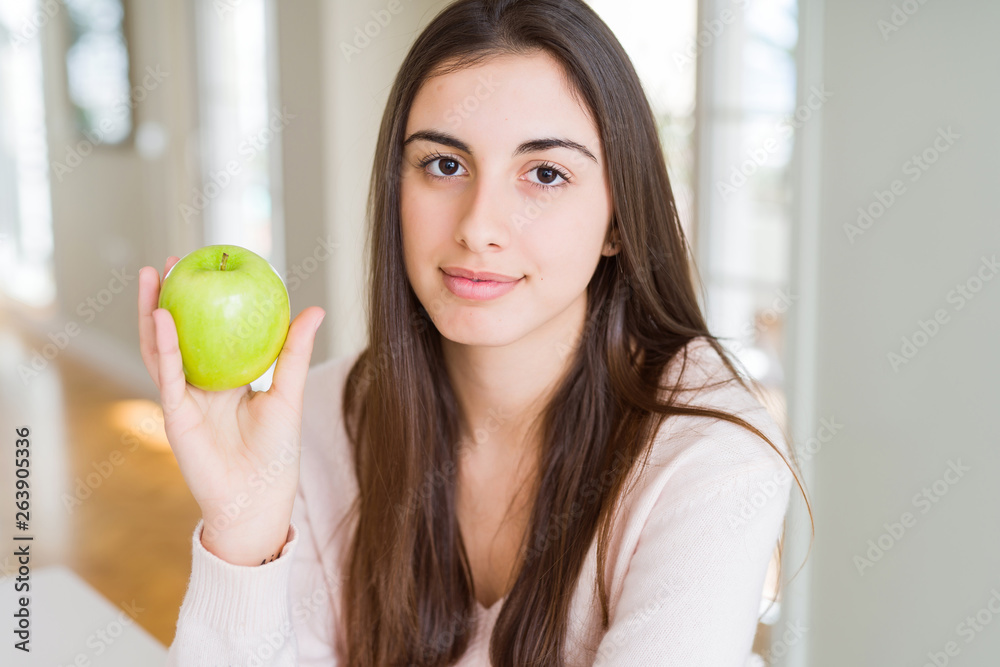 Beautiful young woman eating healthy green apple fruit with a confident expression on smart face thinking serious Beautiful young woman eating healthy green apple fruit with a confident expression on smart face thinking serious
