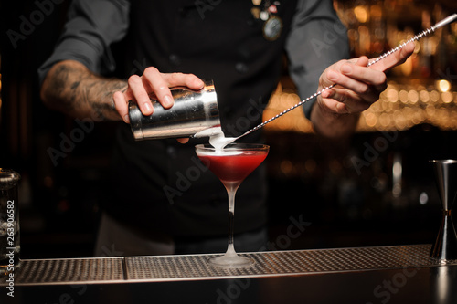 Bartender pouring cocktail using shaker and spoon
