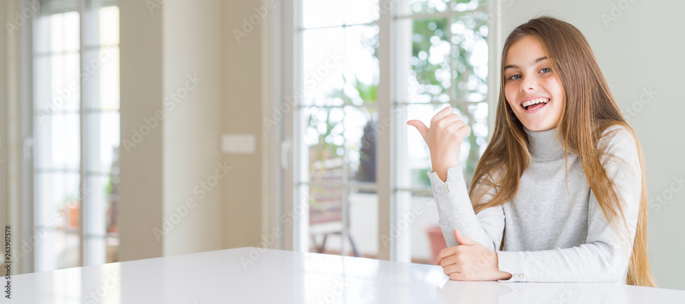 Wide angle picture of beautiful young girl kid wearing casual sweater smiling with happy face looking and pointing to the side with thumb up. Wide angle picture of beautiful young girl kid wearing casual sweater smiling with happy face looking and pointing to the side with thumb up.