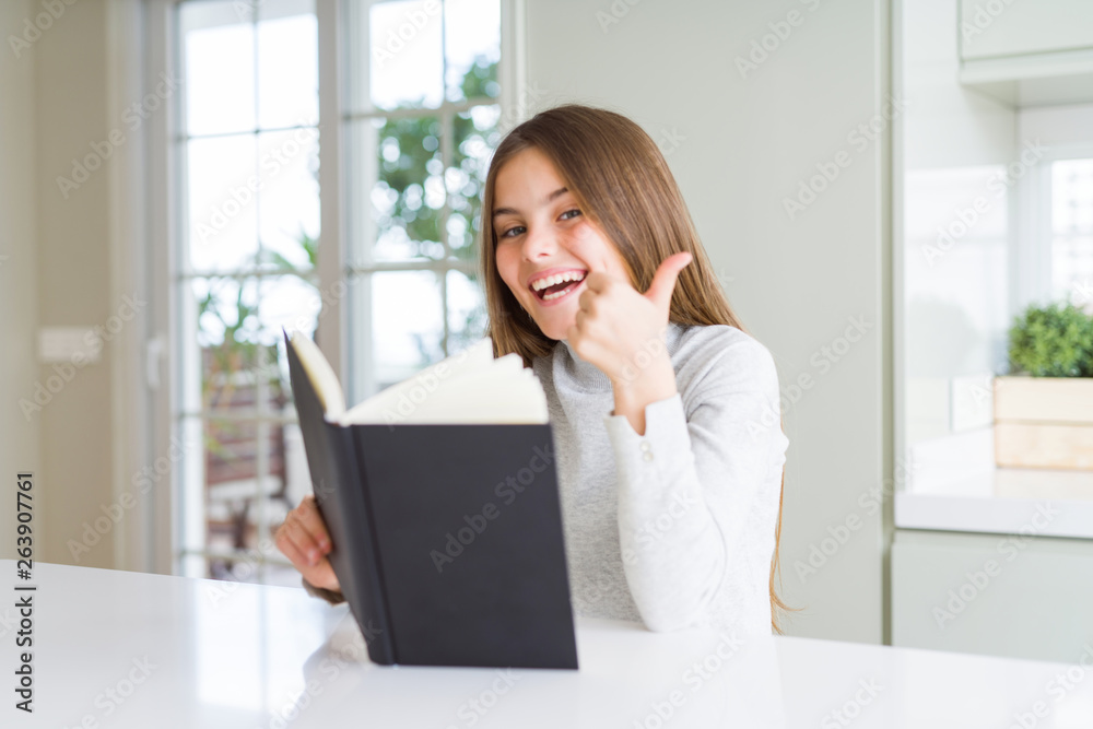 Beautiful young girl reading a book at home happy with big smile doing ok sign, thumb up with fingers, excellent sign Beautiful young girl reading a book at home happy with big smile doing ok sign, thumb up with fingers, excellent sign