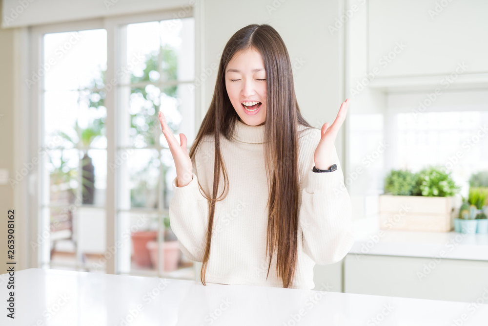 Beautiful Asian woman wearing casual sweater celebrating mad and crazy for success with arms raised and closed eyes screaming excited. Winner concept Beautiful Asian woman wearing casual sweater celebrating mad and crazy for success with arms raised and closed eyes screaming excited. Winner concept