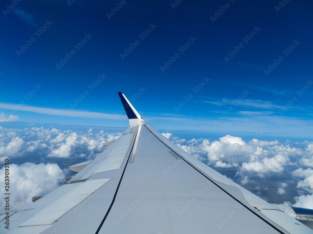 Wing of an airplane above the clouds with a bright blue sky on a sunny day.