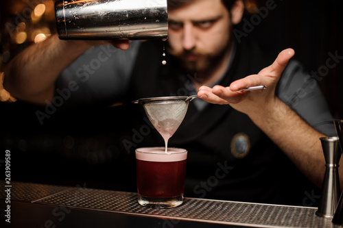 Bartender prepares alcohol drink with a shaker and sieve