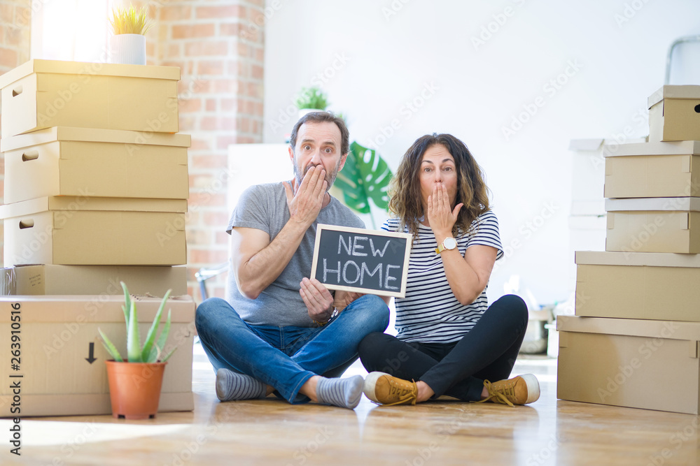 Middle age senior couple sitting on the floor holding blackboard moving to a new home cover mouth with hand shocked with shame for mistake, expression of fear, scared in silence, secret concept Middle age senior couple sitting on the floor holding blackboard moving to a new home cover mouth with hand shocked with shame for mistake, expression of fear, scared in silence, secret concept