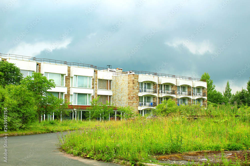 A three-storey house among green trees against a blue cloudy sky