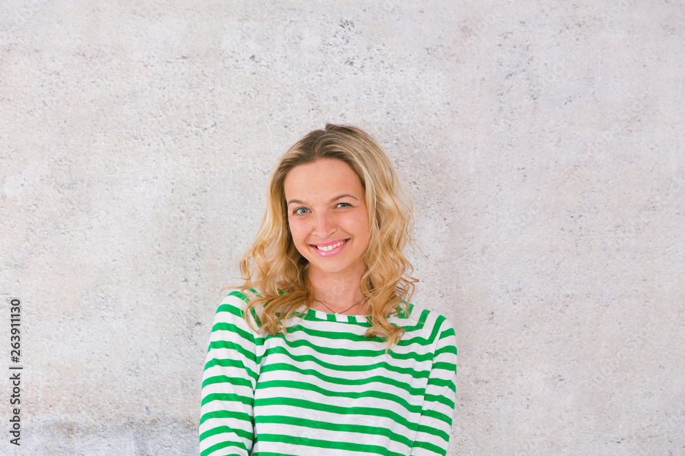 young, pretty blonde woman posing in front of a concrete wall and wearing green, white striped sweaters